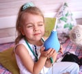 Caucasian little girl with stethoscope at home playing doctor with big blue enema to treat a bear. Little therapist. Coronavirus Royalty Free Stock Photo