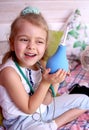 Caucasian little girl with stethoscope at home playing doctor with big blue enema to treat a bear. Little therapist. Coronavirus Royalty Free Stock Photo