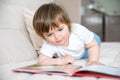 Caucasian little girl of two years with blue eyes in a white T-shirt lies on a sofa with a book.