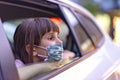 Caucasian little girl wearing mask looking out of the open window of a car.