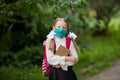 Caucasian little girl in a white blouse, with a briefcase. In the hands of a school book. A cute student in a medical mask. Royalty Free Stock Photo