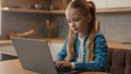 Caucasian little school girl child baby kid schoolgirl daughter at home kitchen using laptop browsing chatting study Royalty Free Stock Photo