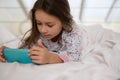 Caucasian lovey little child girl in nightwear, watching cartoons on mobile phone before sleeping, lying down on her bed