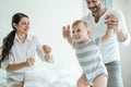 Caucasian loving parents play with baby boy child on bed in bedroom. Happy family, attractive beautiful young couple dad and mom Royalty Free Stock Photo