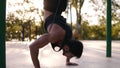 Caucasian male athlete doing push ups while standing on his head with bands insurance. Training on the local sportyard