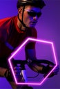 Caucasian male athlete wearing helmet and eyewear riding bike by illuminated hexagon, copy space