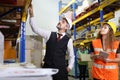 Caucasian male boss is checking for the stock inventory inside warehouse with his female store manager in full safety equipment