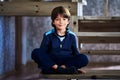 Caucasian male child of seven years old sits cross-legged on step of wooden staircase at home. Royalty Free Stock Photo