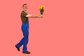 Caucasian male courier holding bouquet. Flower delivery concept. Man in workers overalls holds out flowers. Side view. Copy space
