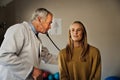 Caucasian male Doctor diagnosing female patients illness in consultation room, stethoscope lung test, deep breathing