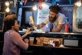 Caucasian male employee in fast food service smiling and talking to a afro-american female customer while adding mustard in her