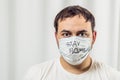 Caucasian male European looking at the camera. In a medical mask and a white T-shirt. Mask Lettering Stay Home