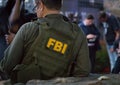 Caucasian male FBI agent wearing glasses in a green bulletproof vest with FBI logo seen from behind on the investigation