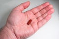 Caucasian male hand holding a red medical capsule pill isolated on white top view Royalty Free Stock Photo