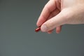 Caucasian male hand holding a red medicine capsule pill between fingers close up shot isolated studio shot Royalty Free Stock Photo