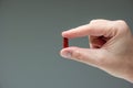 Caucasian male hand holding a red medicine capsule pill between fingers close up shot isolated studio shot Royalty Free Stock Photo