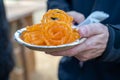 Caucasian male hand holds a plate of Jalebi tradtional Indian fried sweet dessert at a festival, in selective focus