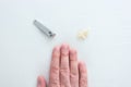 Caucasian male hand next to a metal nail clipper and some cut finger and toe nails in a triangle arrangement on a white surface