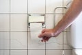 Caucasian male hand reaching for a nearly empty toilet roll next to a partially visible toilet basin and metal plumbing Royalty Free Stock Photo