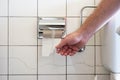 Caucasian male hand reaching for a nearly empty toilet roll next to a partially visible toilet basin and metal plumbing Royalty Free Stock Photo