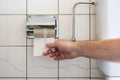 Caucasian male hand reaching for a nearly empty toilet roll next to a partially visible toilet basin and metal plumbing Royalty Free Stock Photo