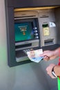 Male hands holding euro banknotes against silver ATM after cash disbursement