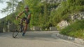 Caucasian male road cyclist pedalling up a steep asphalt road in sunny woods.