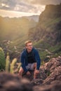 A caucasian male sitting on the edge of  green cliff and thinking with green hills in the background Royalty Free Stock Photo