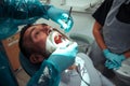 Caucasian male sitting with mouth wide open while male dentist cleans teeth