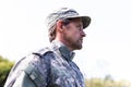 Caucasian male soldier wearing camo fatigues and cap standing outdoors looking away