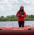 Caucasian male stands confidently on a red inflatable raft in a body of water