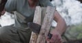 Caucasian male survivalist using branch and machete to cleave firewood at camp in wilderness