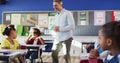 Caucasian male teacher walking through classroom checking excersise of diverse children
