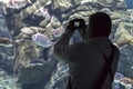 Caucasian male tourist holding a digital camera is taking photos of various species of fishes at `Cretaquarium` in Heraklion city