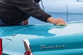 caucasian male uses a cloth to clean a blue Ford Thunderbird classic car