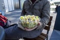 Caucasian male in a winter jacket, holding out a southwestern salad in a plastic to-go container at an outdoor table