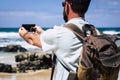 Caucasian man with backpack taking picture with mobile phone technology device to the beach and ocean waves - people enjoying Royalty Free Stock Photo