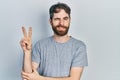 Caucasian man with beard wearing casual grey t shirt smiling with happy face winking at the camera doing victory sign Royalty Free Stock Photo