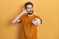 Caucasian man with beard wearing casual yellow t shirt smiling doing talking on the telephone gesture and pointing to you Royalty Free Stock Photo
