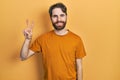 Caucasian man with beard wearing casual yellow t shirt smiling looking to the camera showing fingers doing victory sign Royalty Free Stock Photo