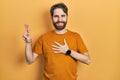 Caucasian man with beard wearing casual yellow t shirt smiling swearing with hand on chest and fingers up, making a loyalty Royalty Free Stock Photo
