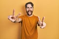 Caucasian man with beard wearing casual yellow t shirt smiling with tongue out showing fingers of both hands doing victory sign Royalty Free Stock Photo