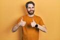 Caucasian man with beard wearing casual yellow t shirt success sign doing positive gesture with hand, thumbs up smiling and happy Royalty Free Stock Photo