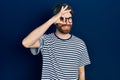 Caucasian man with beard wearing striped t shirt and glasses doing ok gesture with hand smiling, eye looking through fingers with Royalty Free Stock Photo