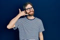 Caucasian man with beard wearing striped t shirt and glasses smiling doing phone gesture with hand and fingers like talking on the Royalty Free Stock Photo