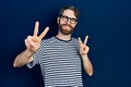 Caucasian man with beard wearing striped t shirt and glasses smiling looking to the camera showing fingers doing victory sign Royalty Free Stock Photo