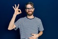 Caucasian man with beard wearing striped t shirt and glasses smiling positive doing ok sign with hand and fingers Royalty Free Stock Photo