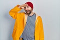 Caucasian man with beard wearing yellow raincoat very happy and smiling looking far away with hand over head Royalty Free Stock Photo