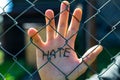 Caucasian man behind wired fence showing hes palm with the word hate