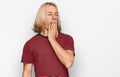 Caucasian man with blond long hair wearing casual striped t shirt bored yawning tired covering mouth with hand